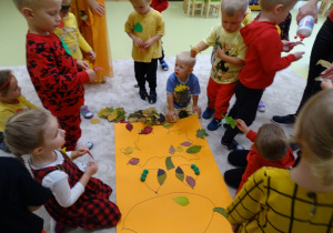 Dzieci ozdabiają krasnala liśćmi.